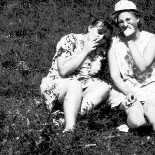 Two people sitting closely outdoors in grassy field.