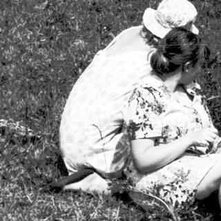 Two people sitting closely in grassy field.