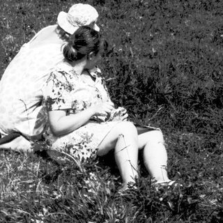 Two people sitting closely in grassy field.