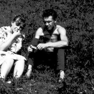 Two people sitting together outdoors in grassy field.