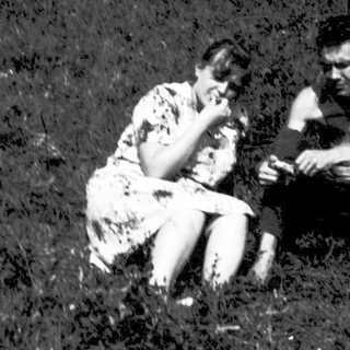 Two people sitting together outdoors in grassy field.