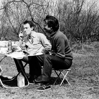 Three men camping, eating outdoors by a fire.
