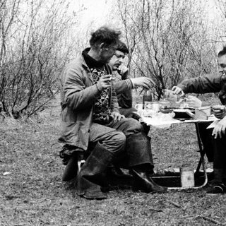 Two men camping, sharing a meal outdoors.