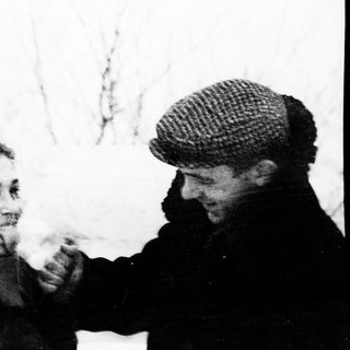 Two people sharing a cigarette outdoors in winter attire.