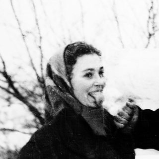 Two people sharing a cigarette outdoors in winter attire.
