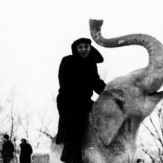 Person posing with large ice elephant sculpture.