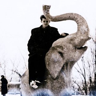 Person sitting atop large elephant statue outdoors.