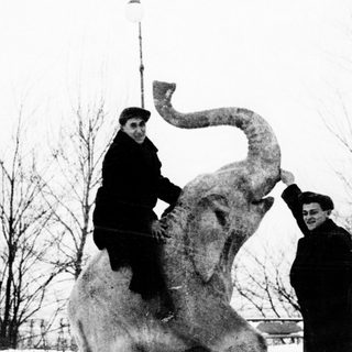 Two men pose with a large elephant statue.