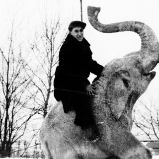 Two men pose with a large elephant statue.