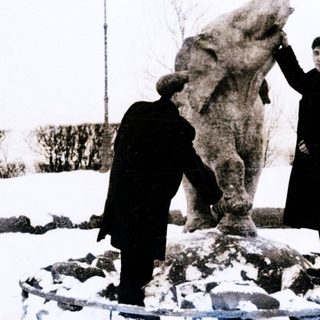 Two men inspecting a large elephant statue in snowy outdoor setting.