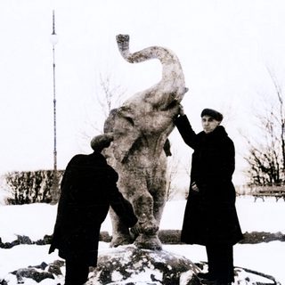 Two men inspecting a large elephant statue in snowy outdoor setting.