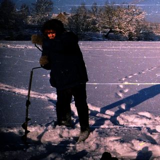 Two people ice fishing on a snow-covered lake at night.
