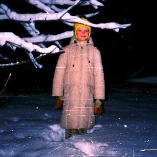 Person in winter coat and hat stands alone on snow-covered ice.