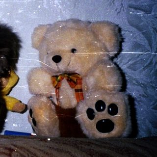 Kitten resting beside a teddy bear on a couch.