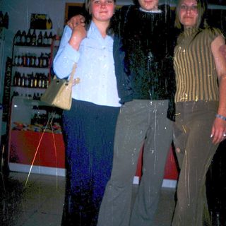 Three people posing indoors near racks of bottles.