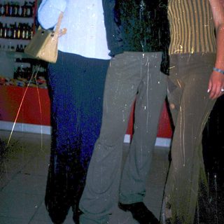 Three people posing indoors near racks of bottles.