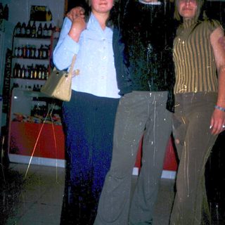 Three people posing indoors near racks of bottles.
