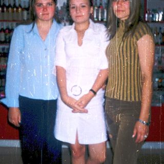 Three women posing indoors near liquor shelves.