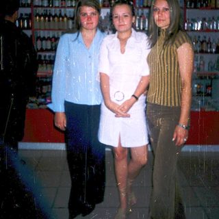 Three women posing indoors near liquor shelves.
