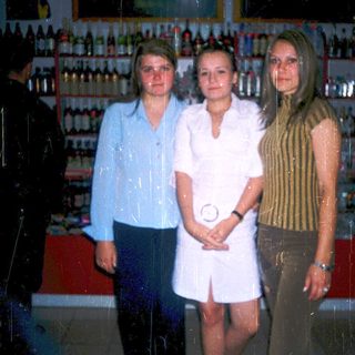 Three women posing indoors near liquor shelves.