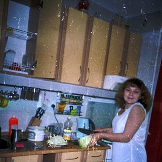 Woman preparing food in cluttered kitchen.