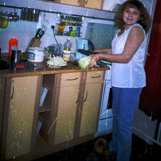 Woman preparing food in cluttered kitchen.