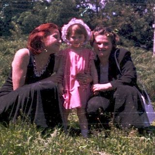 Three people sitting together outdoors in vintage clothing.