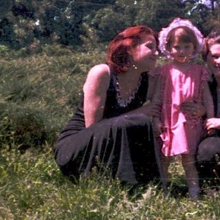 Three people sitting together outdoors in vintage clothing.