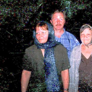 Three people standing outdoors at night in rain.