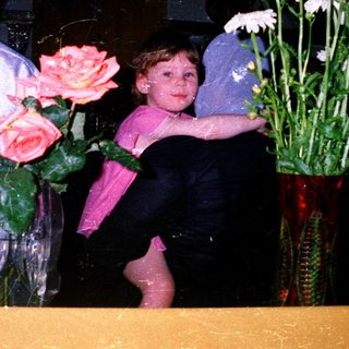 Child holding flowers with adult in background.