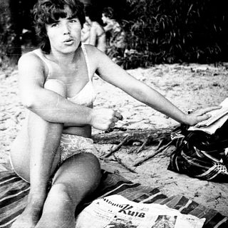 Woman sitting shirtless on beach towel.