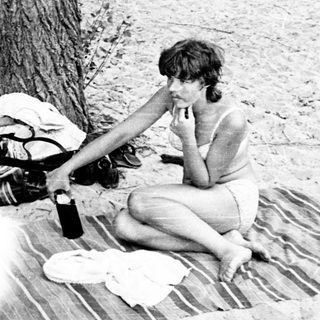 Woman sitting on blanket outdoors, drinking.