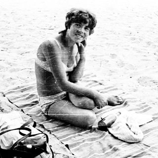 Woman sitting on beach towel with backpack.