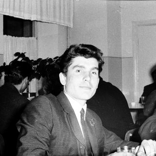 Young man in suit at formal event with cameras.