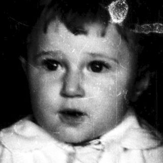 Young child in white outfit holding object near window.
