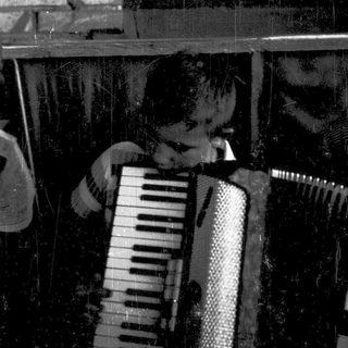 Person playing accordion indoors near brick wall.
