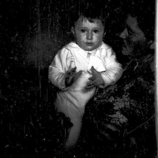 Baby in white outfit crying indoors.