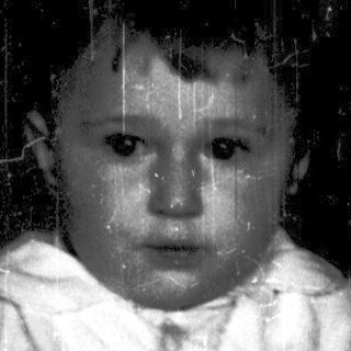 Baby in white outfit crying indoors.