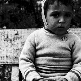 Young child wearing sweater and hood outdoors.