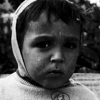 Young child wearing sweater and hood outdoors.