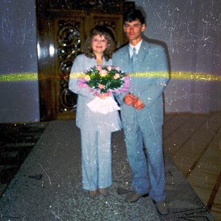 Couple posing with flowers at wedding ceremony entrance.