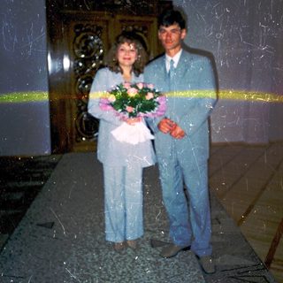 Couple posing with flowers at wedding ceremony entrance.