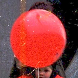 Child blowing red balloon near bear statue.