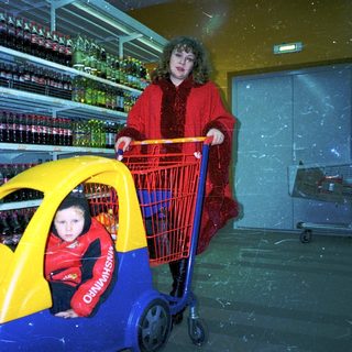A woman pushes a child in a toy car inside a grocery store.