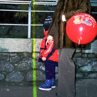 Woman holding red balloon with child near bridge.