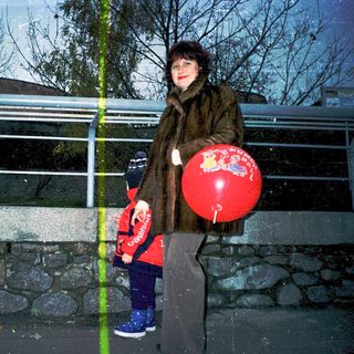 Woman holding red balloon with child near bridge.