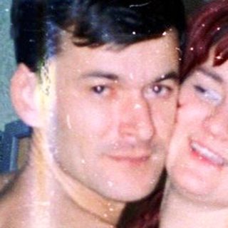 Two people posing indoors, shirtless and holding hands.