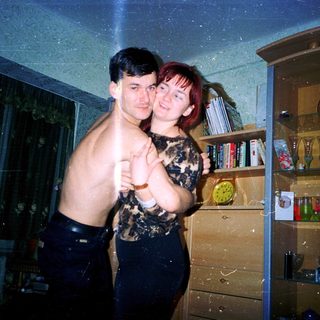 Two people posing indoors, shirtless and holding hands.