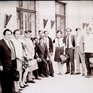Group of people posing outside a building in formal 1960s attire.
