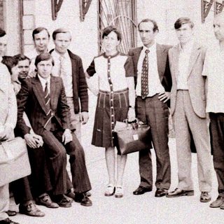 Group of people posing outside a building in formal 1960s attire.